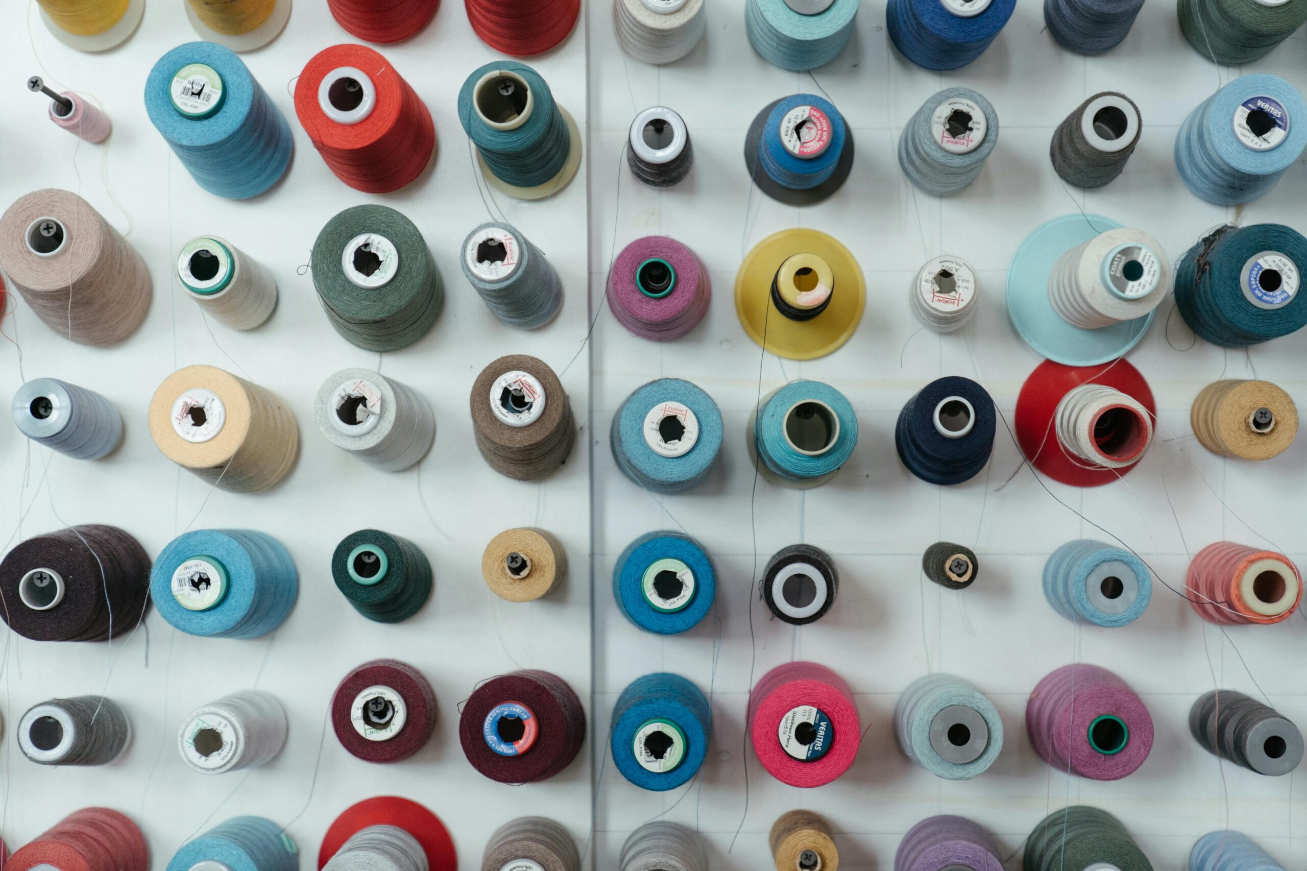 A flat lay of colorful thread spools neatly arranged in a grid, highlighting sewing organization.